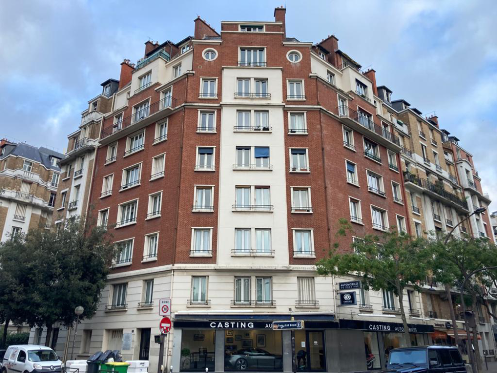 Immeuble d’angle en briques rouges avec des commerces au rez-de-chaussée, sous un ciel nuageux