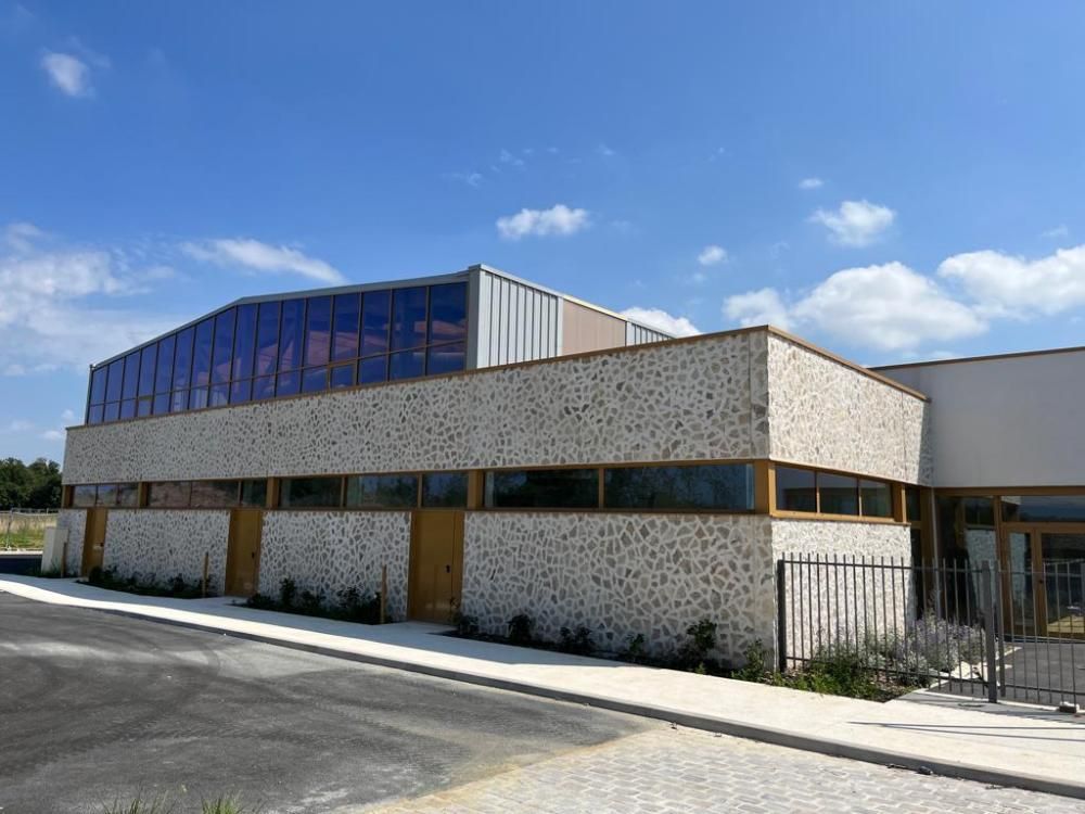 Bâtiment moderne de faible hauteur, avec une façade en briques blanches et des fenêtres supérieures bleues, sous un ciel dégagé.
