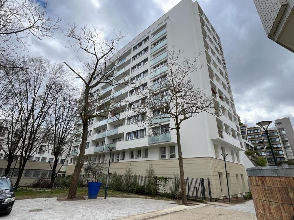 Grand immeuble blanc à côté d’arbres dénudés et de voitures garées, par temps couvert