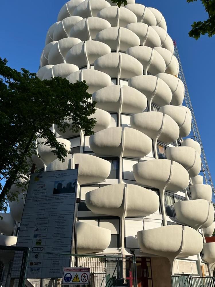 Tour blanche en hauteur, en forme de capsule, avec une enseigne à l’avant, sur fond de ciel bleu dégagé.