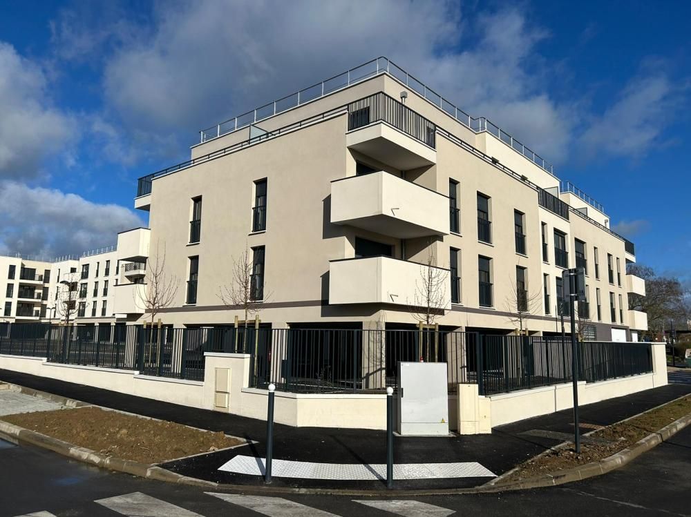 Immeuble d’appartements moderne beige avec des balcons, à l’angle d’une rue sous un ciel bleu