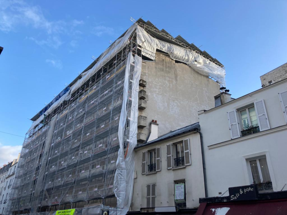 Bâtiment en rénovation, enveloppé d’échafaudages et de filets de protection sur fond de ciel bleu