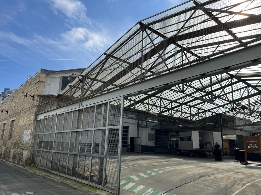 Entrepôt industriel abandonné, avec un toit endommagé et une clôture grillagée, sous un ciel nuageux