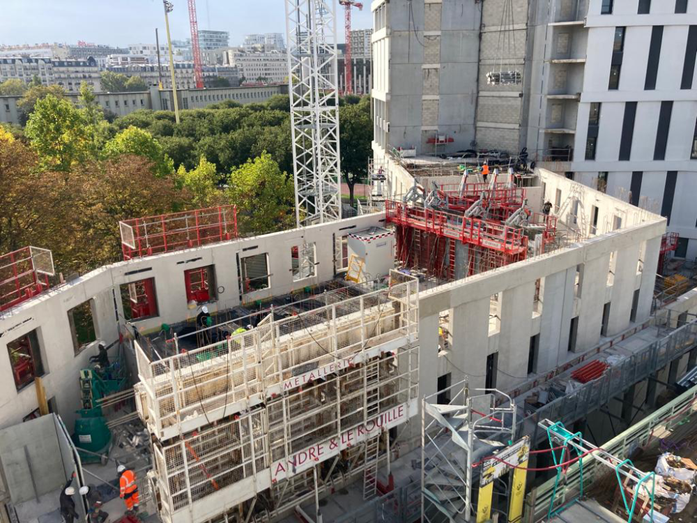 Chantier avec des échafaudages à l’intérieur d’un bâtiment en béton en construction, des ouvriers visibles en contrebas.