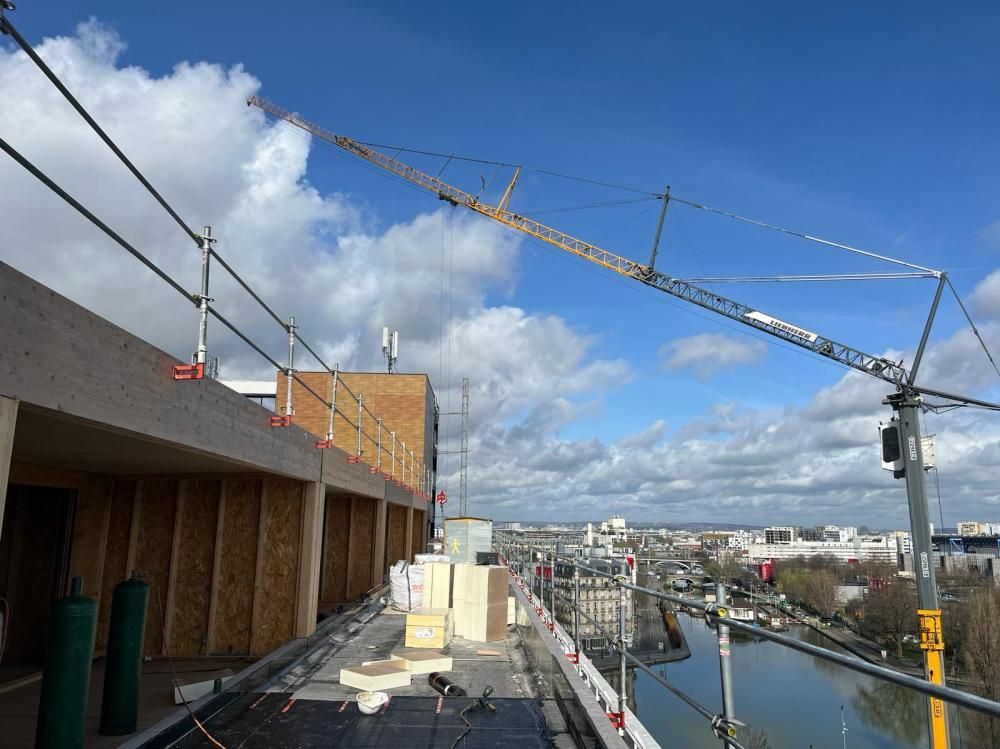 Chantier surplombant un port, avec des grues, des échafaudages et des bâtiments en briques en partie construits sous un ciel bleu