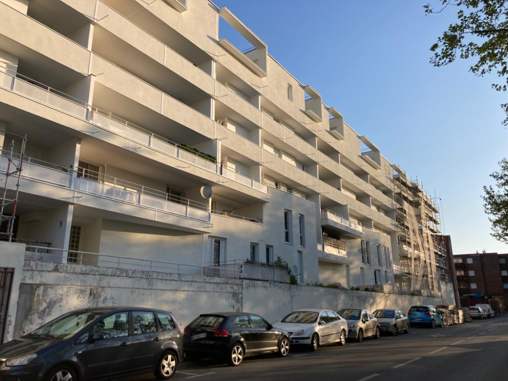 Immeuble ensoleillé avec des balcons et des voitures garées le long de la rue