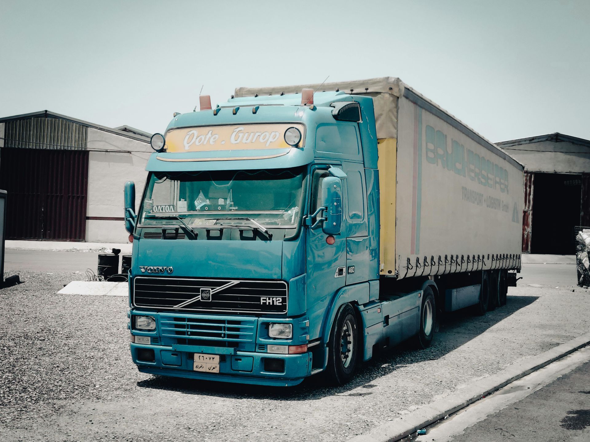 Un camión semirremolque Volvo azul está estacionado en un lote de grava.