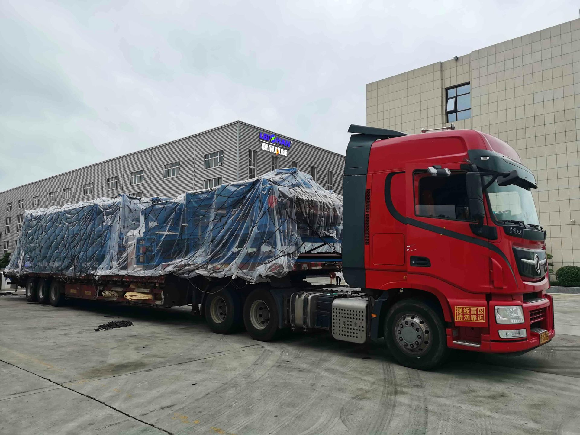Un camión semirremolque rojo está estacionado frente a un edificio.