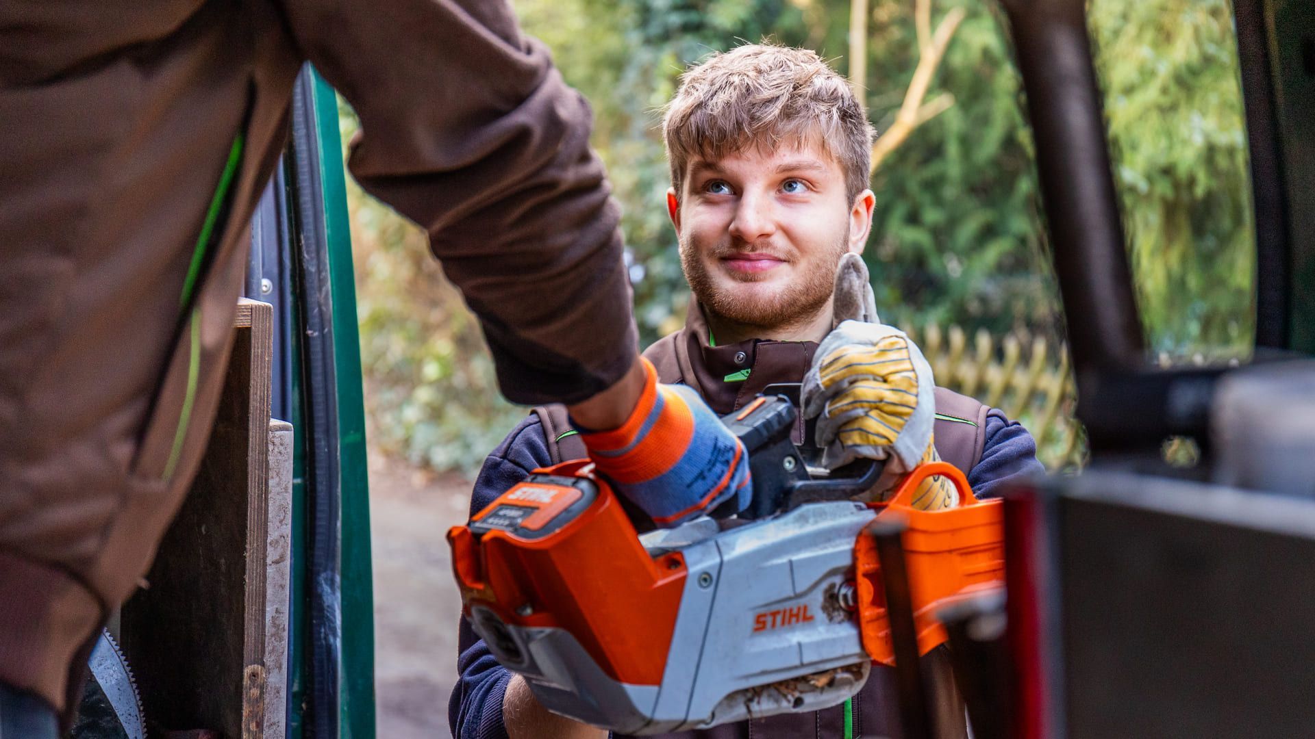 Ein Mann hält eine Kettensäge in der Hand, während er neben einem anderen Mann steht.