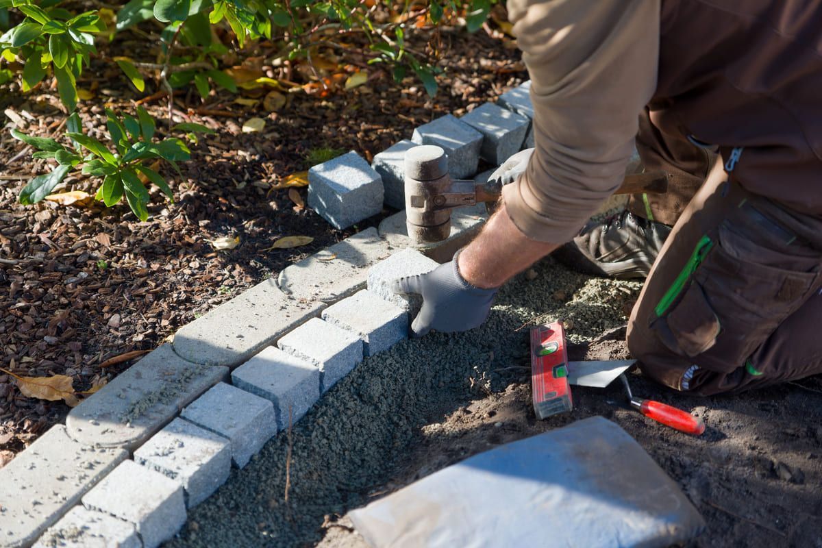 Ein Mann kniet nieder und hämmert mit einem Hammer Ziegelsteine ​​in den Boden.