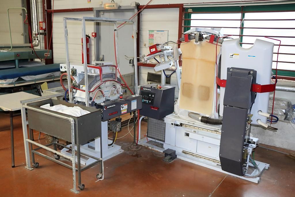 Équipement industriel dans un laboratoire ; des réservoirs métalliques, des tuyaux et un panneau de commande sont visibles.