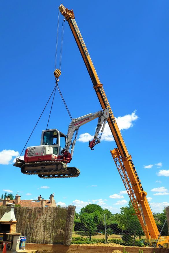 Una grúa levanta una excavadora blanca y roja contra un cielo azul.