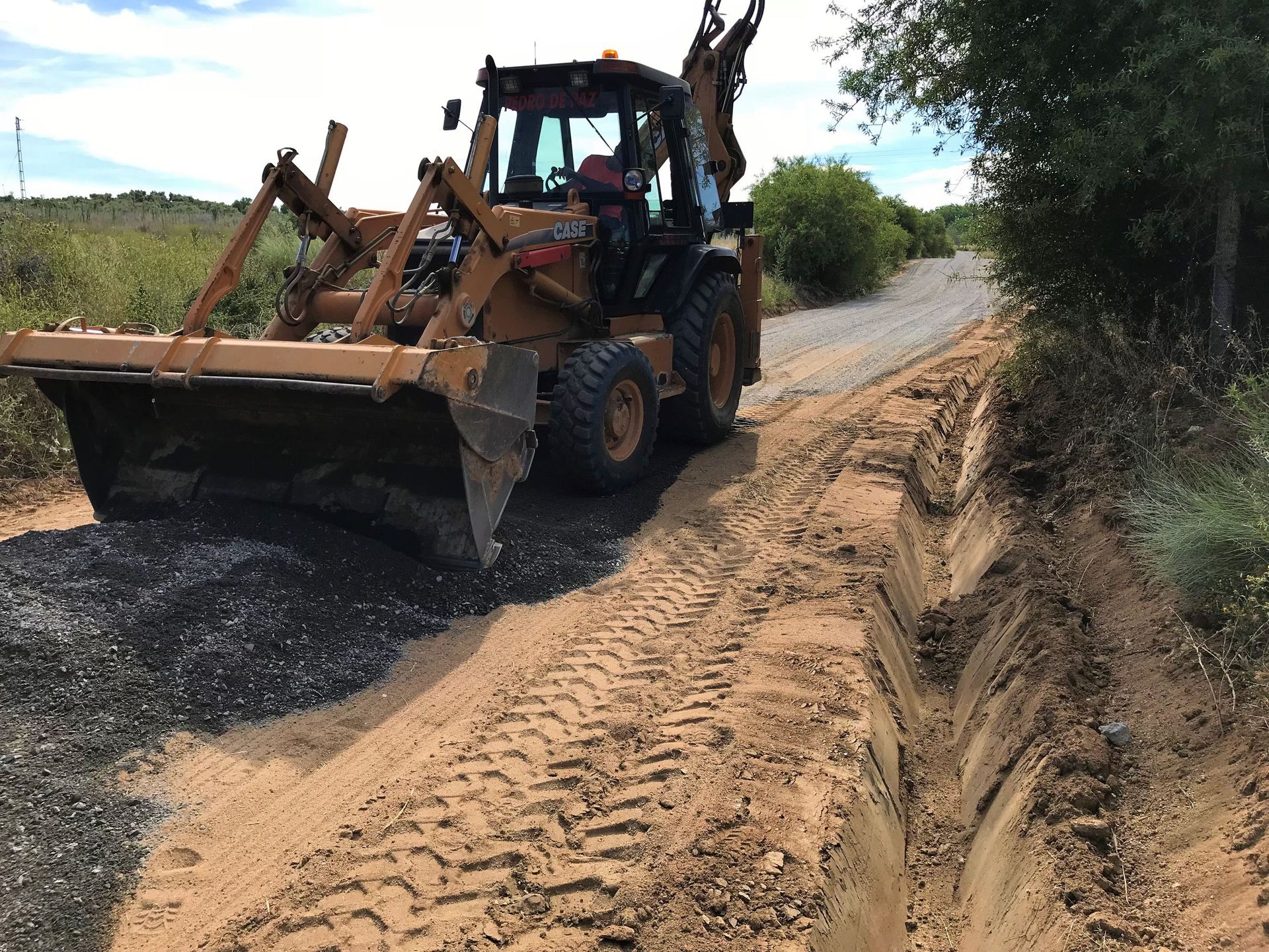 Retroexcavadora nivelando un camino de tierra, esparciendo grava.