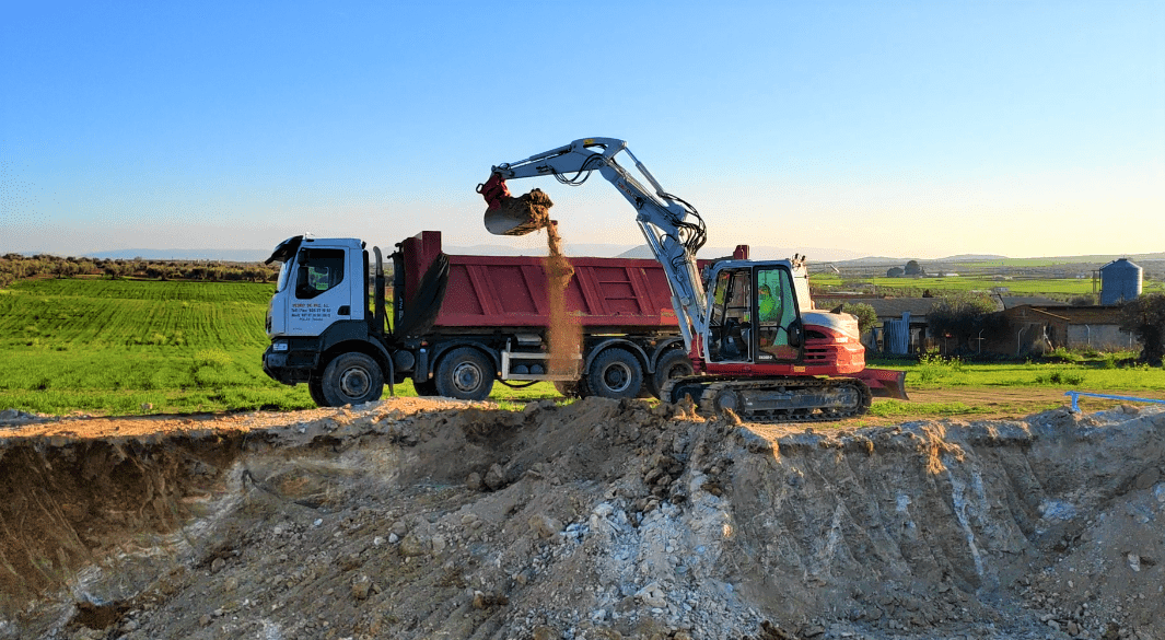 Excavadora cargando tierra en un camión volquete en un sitio de construcción en un día soleado.