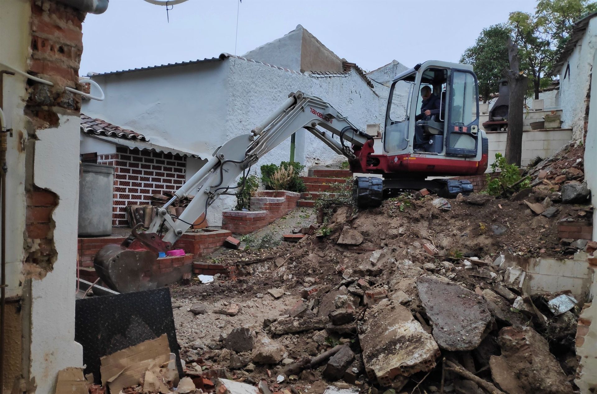 Una excavadora demuele un edificio, dejando visibles escombros y ladrillos a la vista.