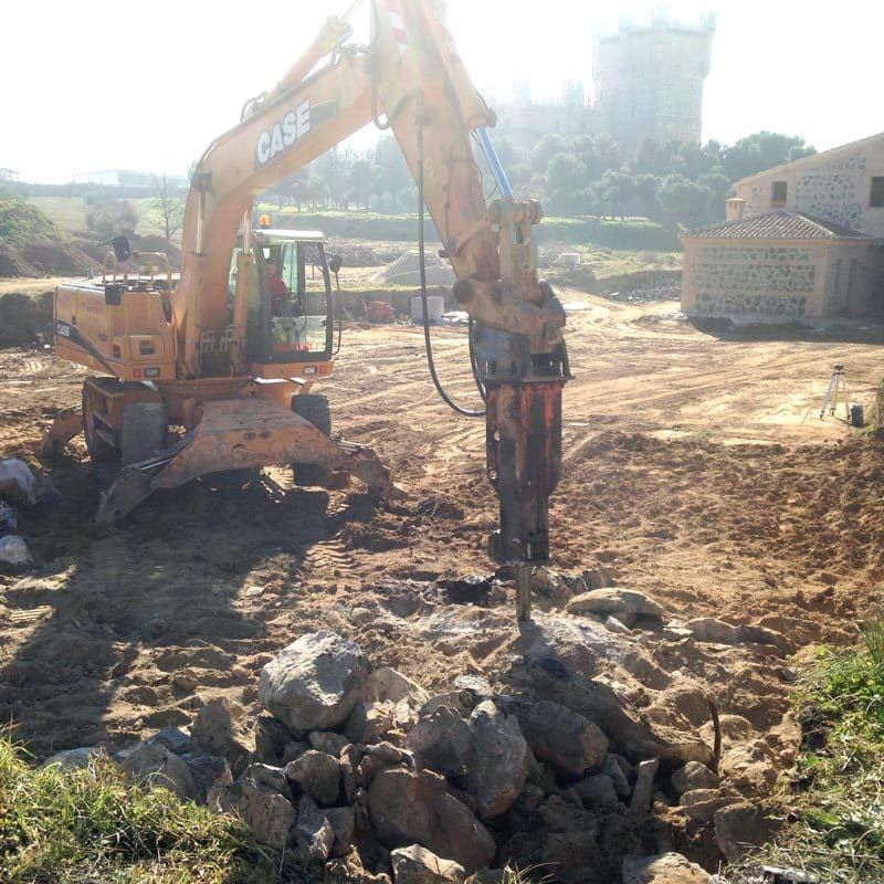 Excavadora con martillo neumático rompiendo rocas en un sitio de construcción.
