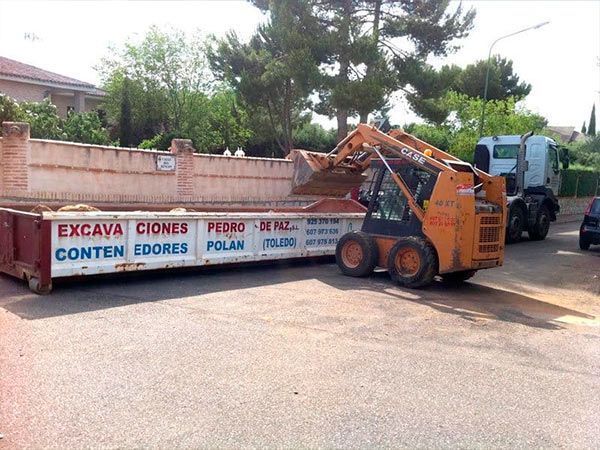 Minicargadora naranja cargando un contenedor grande rotulado 