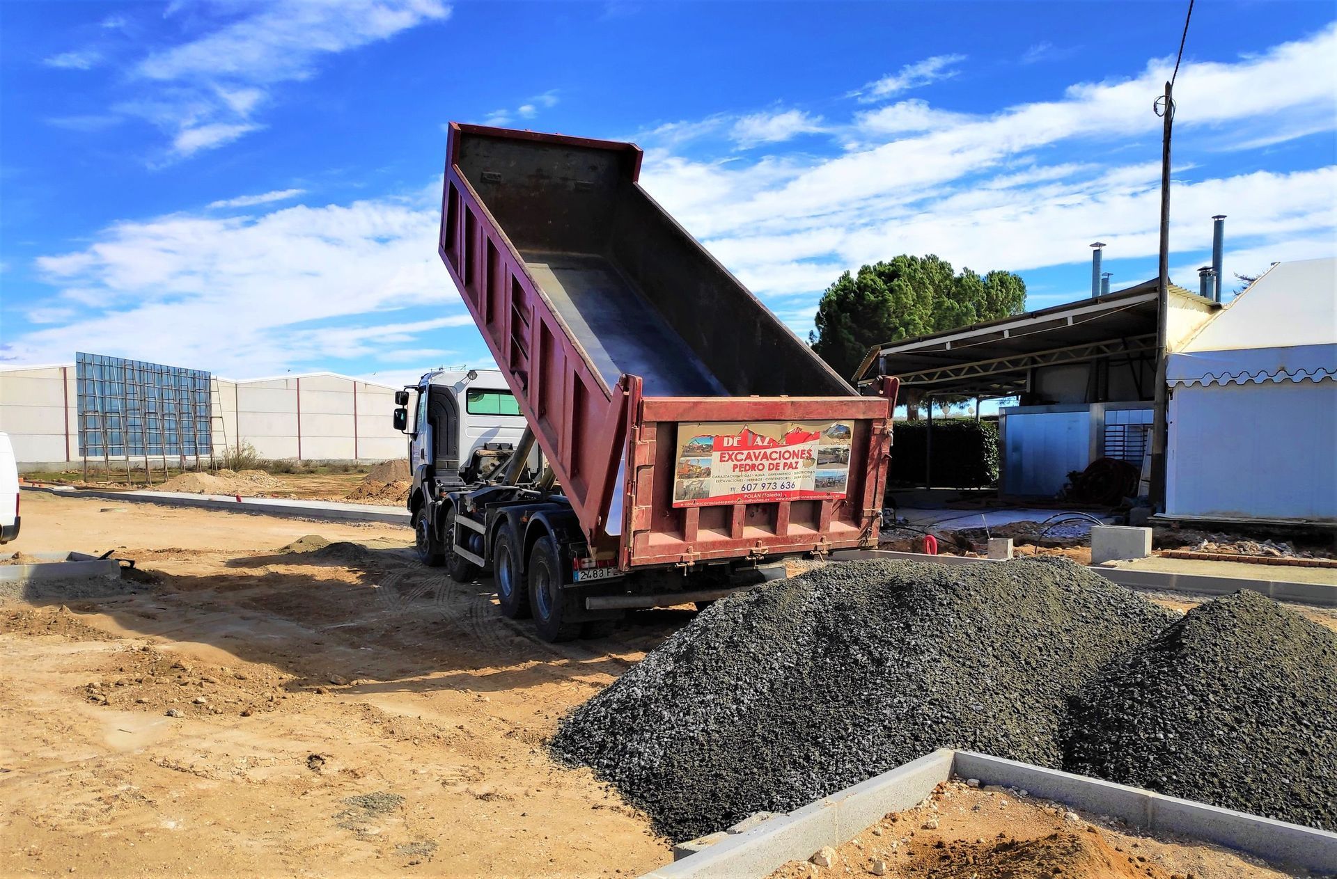Camión volquete descargando grava en un sitio de construcción en un día soleado.