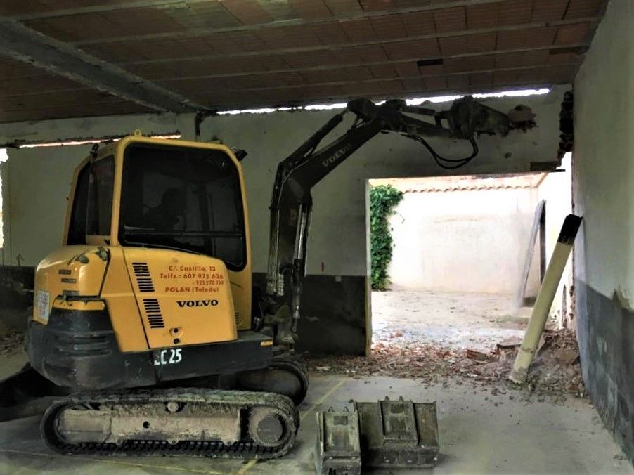Excavadora Volvo amarilla demoliendo una puerta en un edificio, escombros en el suelo.