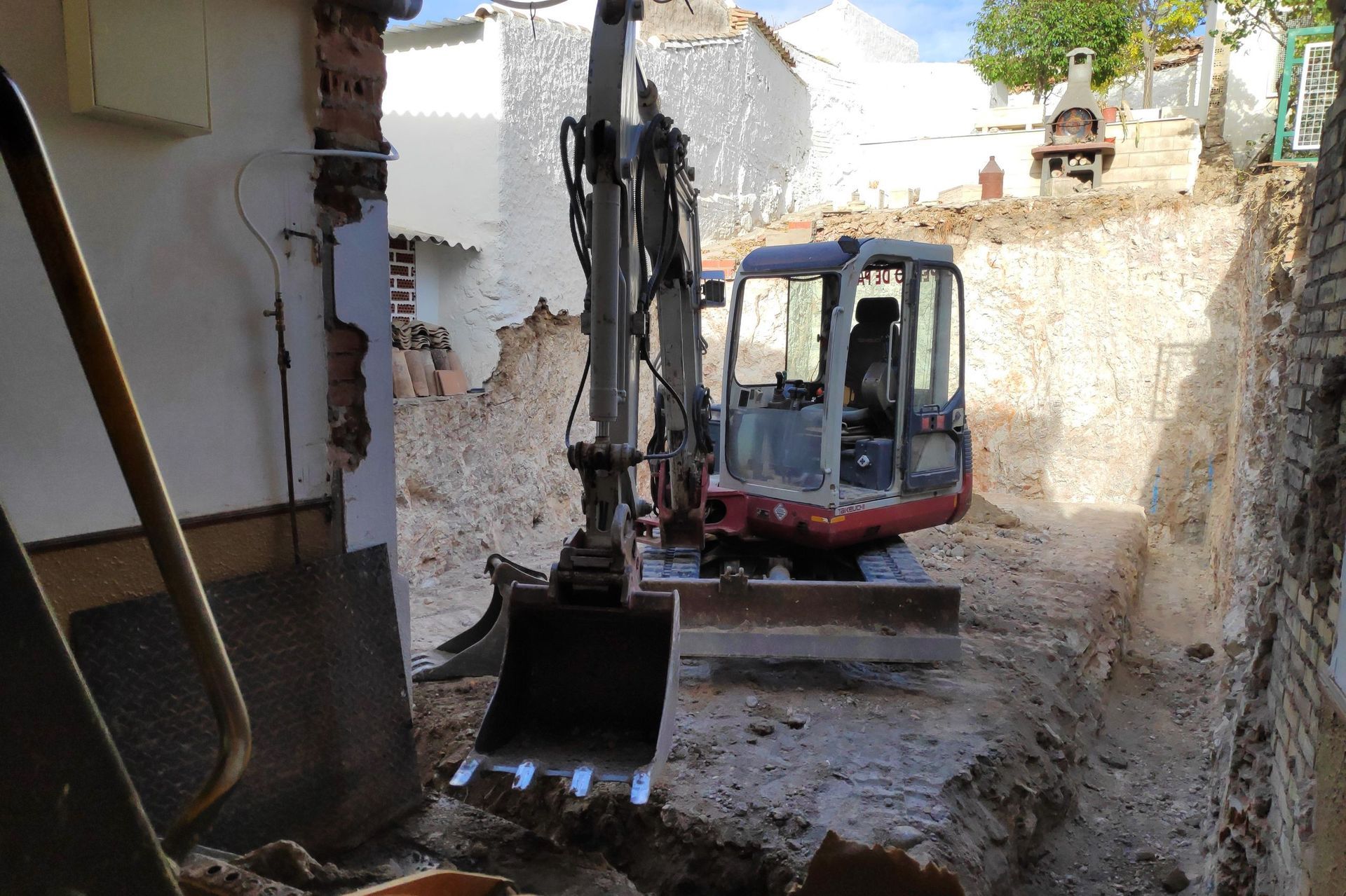 Excavadora en un sitio de construcción, cavando zanja entre paredes de ladrillo y piedra.