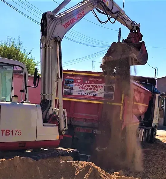 Camión volquete con caja roja descargando grava en un sitio de construcción.