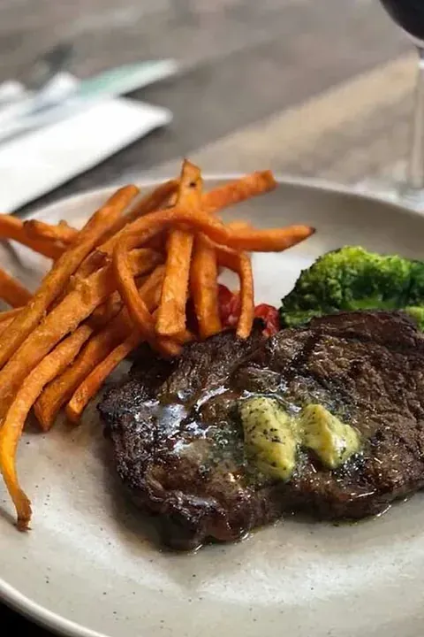 Un plato blanco cubierto con un filete, brócoli y batatas fritas.