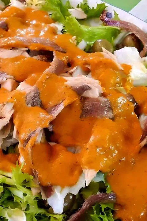 Un primer plano de una ensalada con carne, verduras y salsa en un plato.