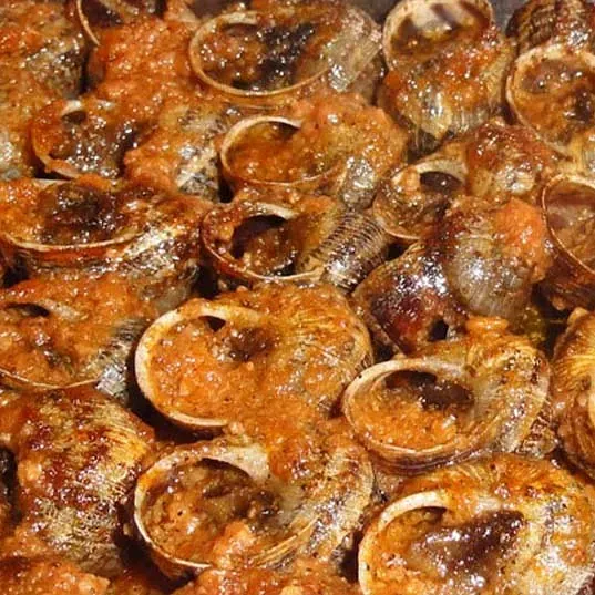 Un primer plano de una pila de caracoles cubiertos de salsa.