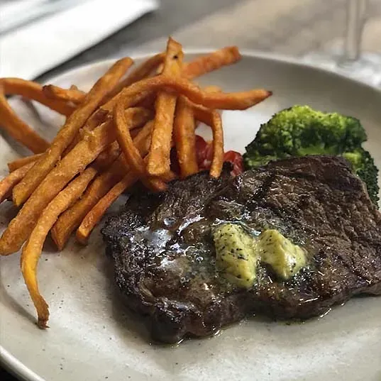 Un plato blanco cubierto con un filete, brócoli y batatas fritas.