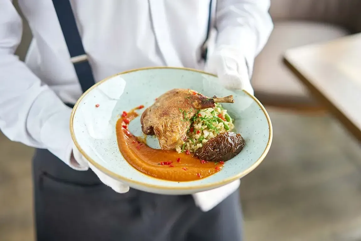 Un camarero sostiene un plato de comida en sus manos.