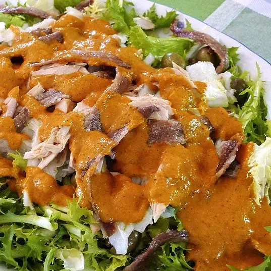Un primer plano de una ensalada con carne y salsa en un plato.
