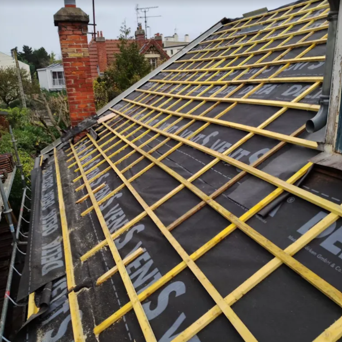 Travaux de toiture en cours avec sous-couche noire et liteaux en bois.