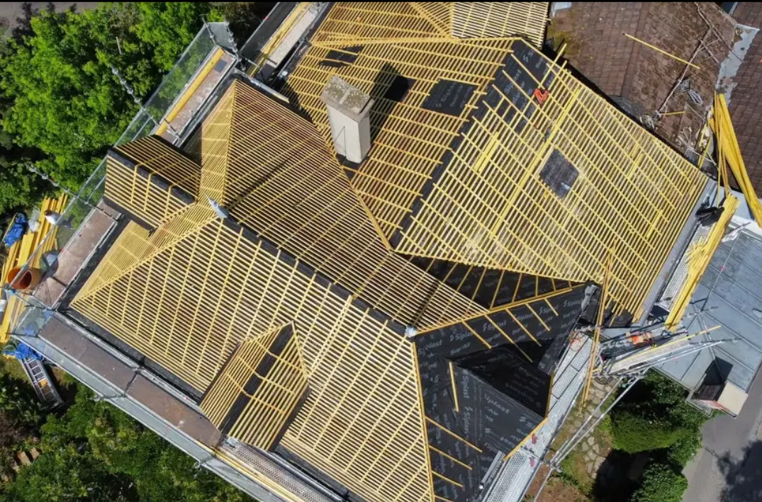 Vue aérienne d'un toit de maison en construction, avec des poutres en bois et une sous-couche sombre.