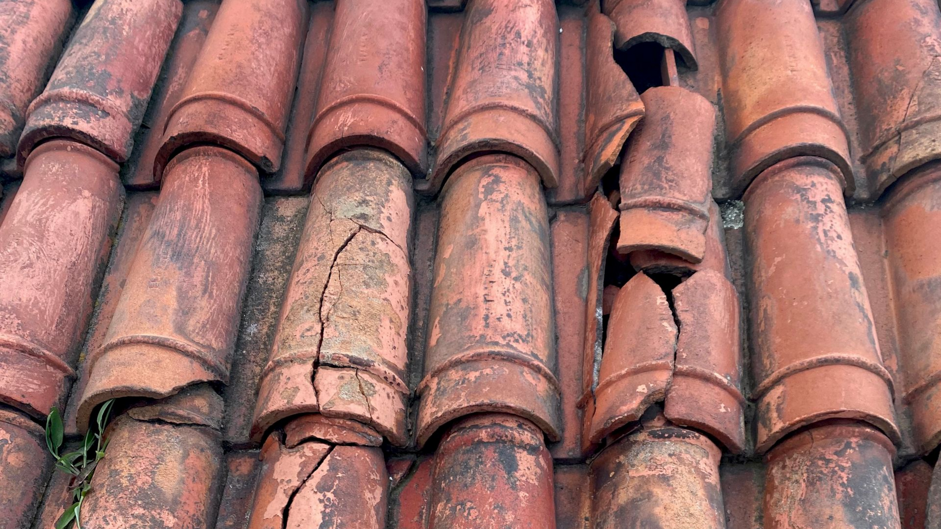 Tuiles de toit en terre cuite rouge fissurées et endommagées.