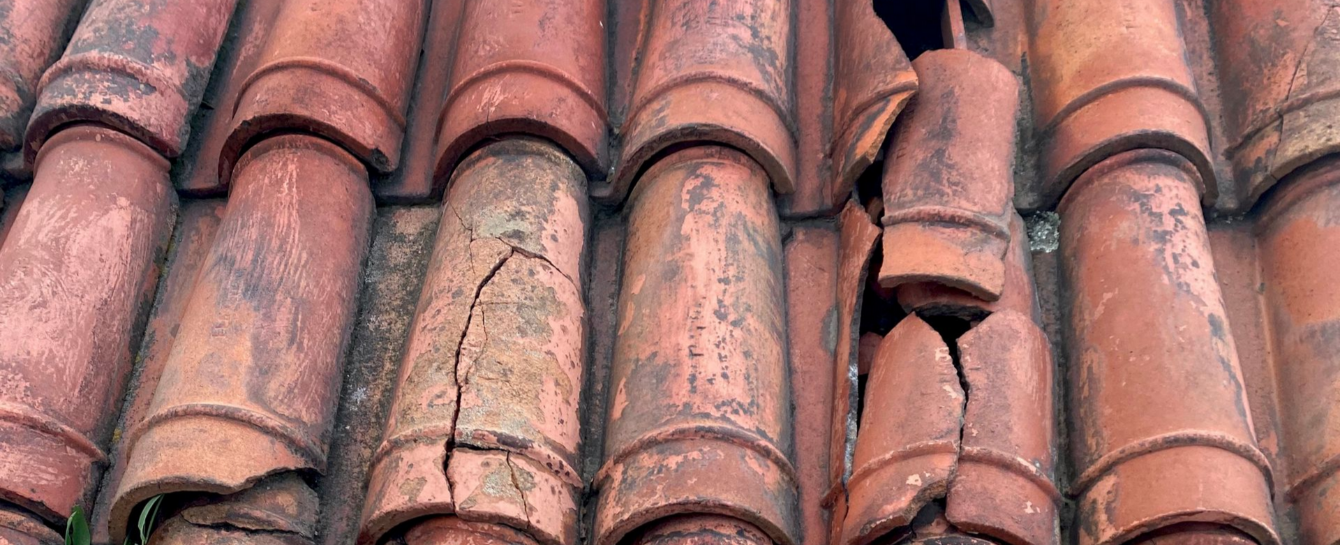 Gros plan sur des tuiles de toit en terre cuite usées par le temps, certaines fissurées et cassées.