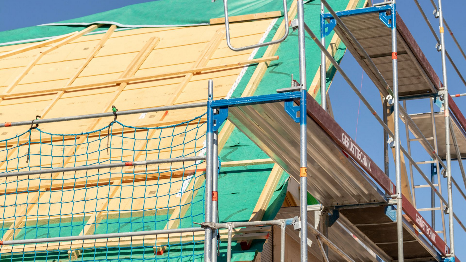 Échafaudages le long d'un bâtiment en construction, bâche verte recouvrant le toit.
