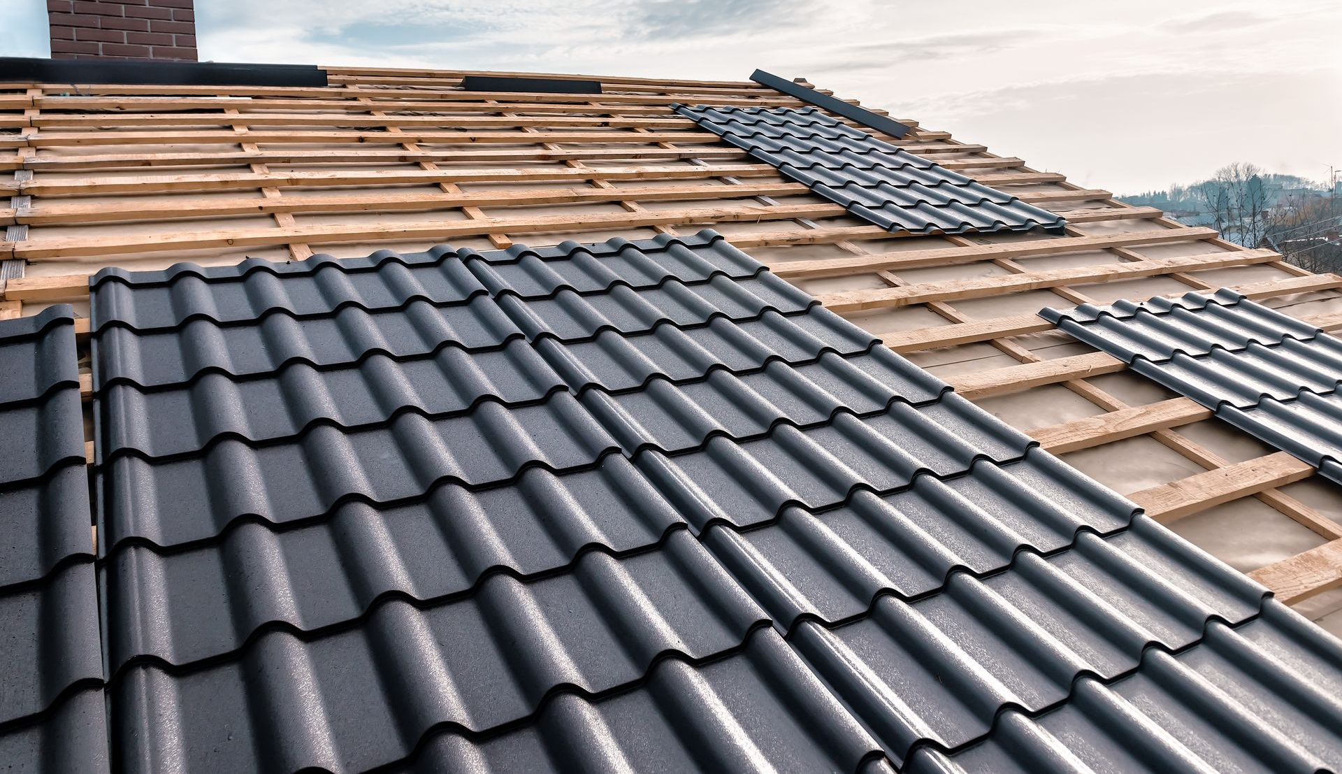 Toiture partiellement recouverte de tuiles gris foncé lors de la pose.