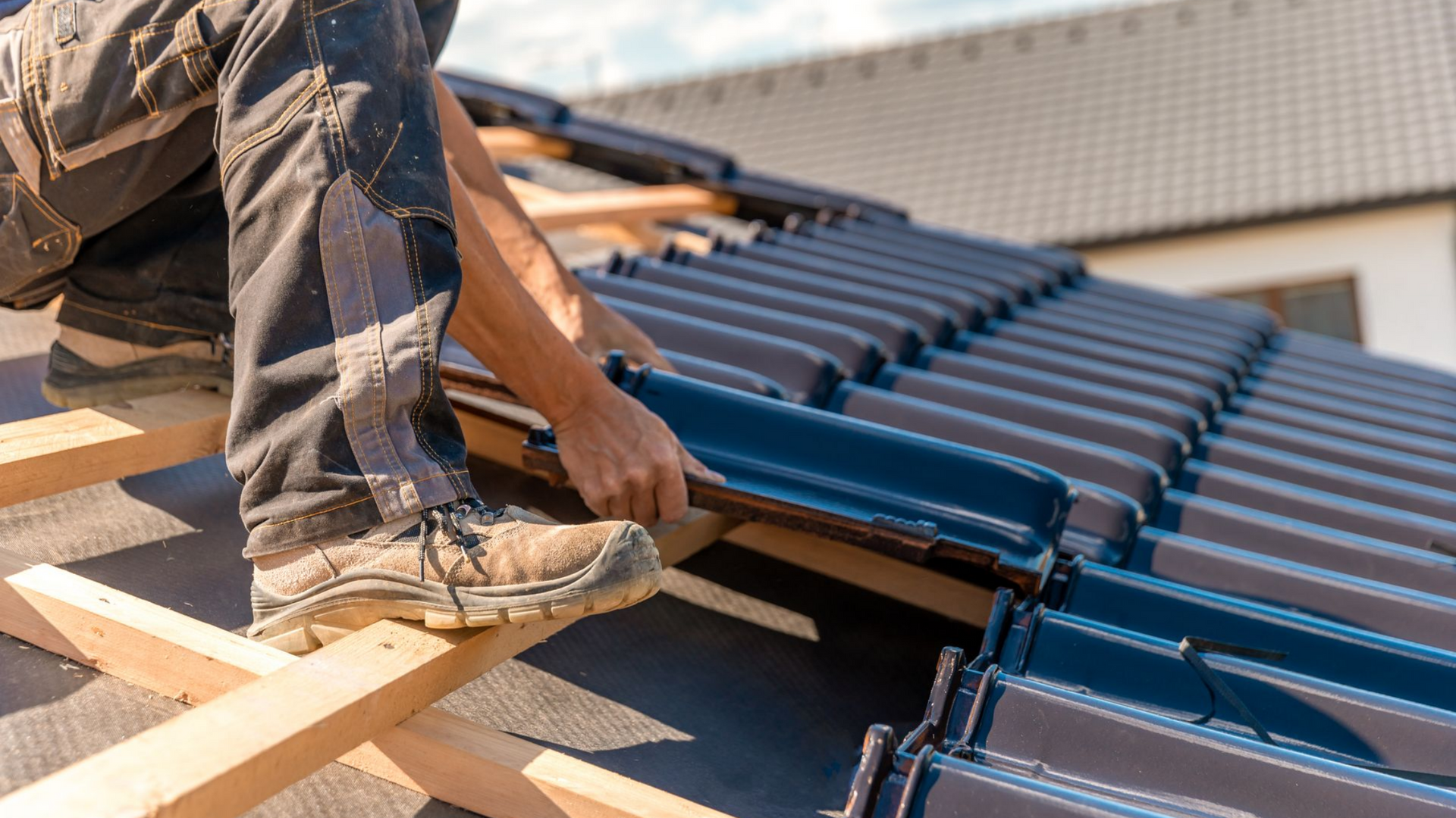 Un couvreur pose des tuiles de toit en céramique bleu foncé sur une charpente en bois.