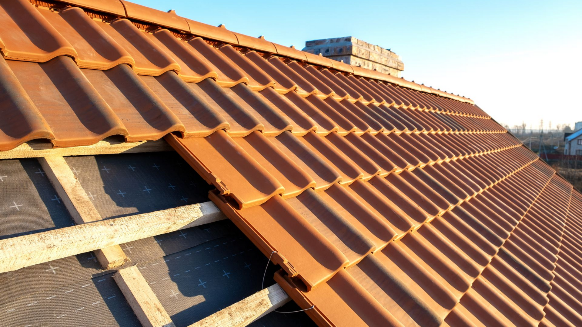 Toiture de tuiles rouges partiellement installée sur un bâtiment en construction.