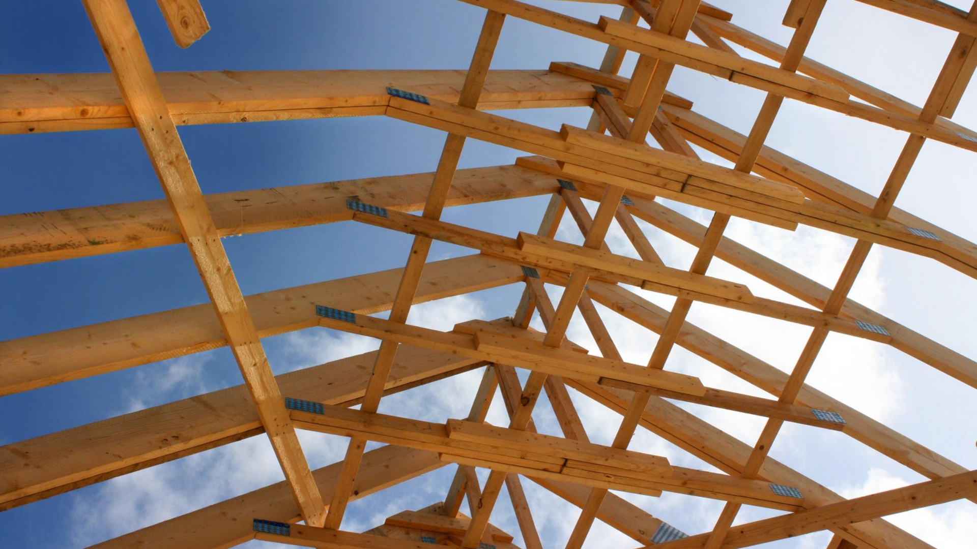 Charpente de toit en bois se détachant sur un ciel bleu.