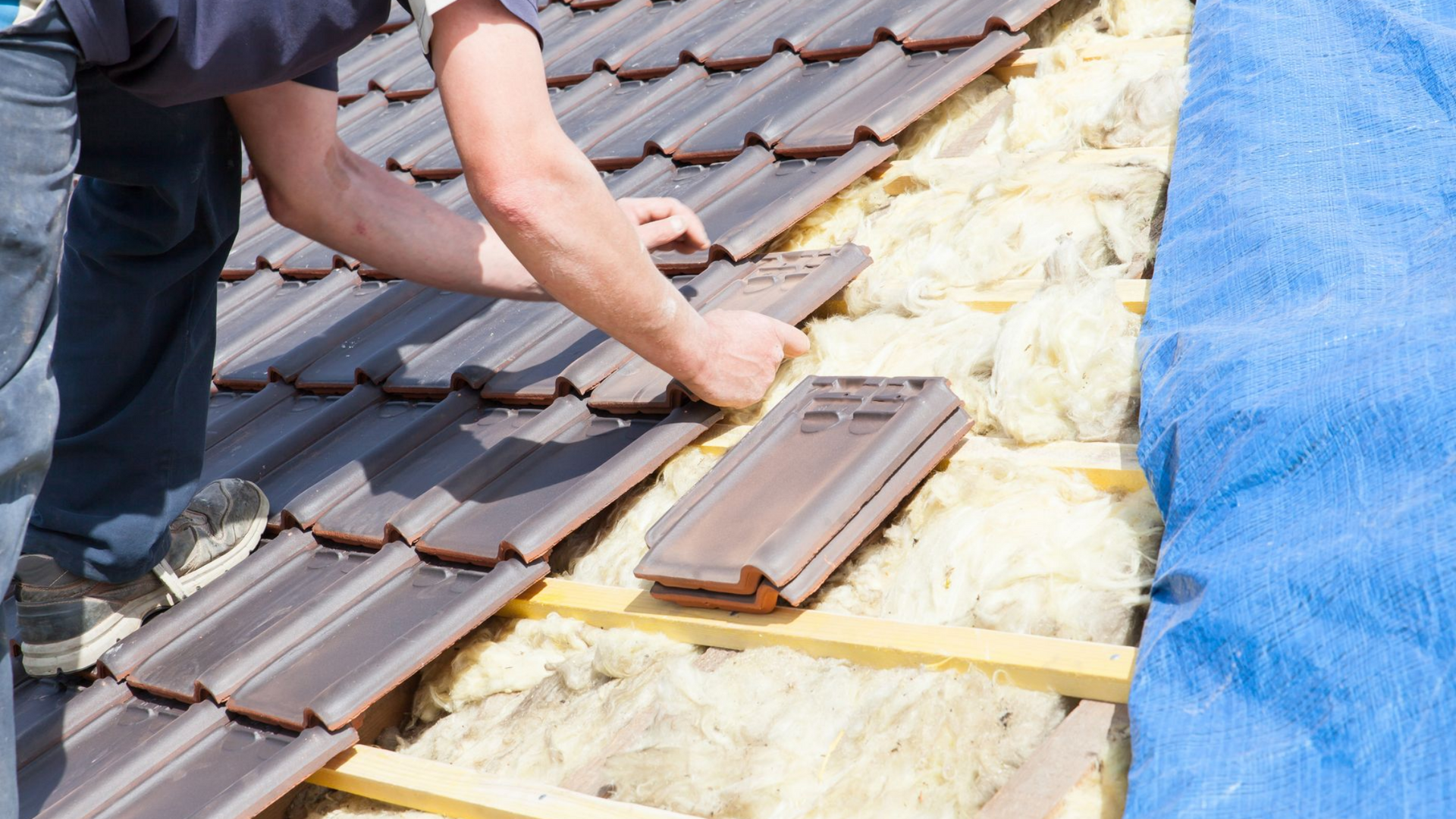 Un couvreur pose des tuiles brunes sur une charpente en bois isolée