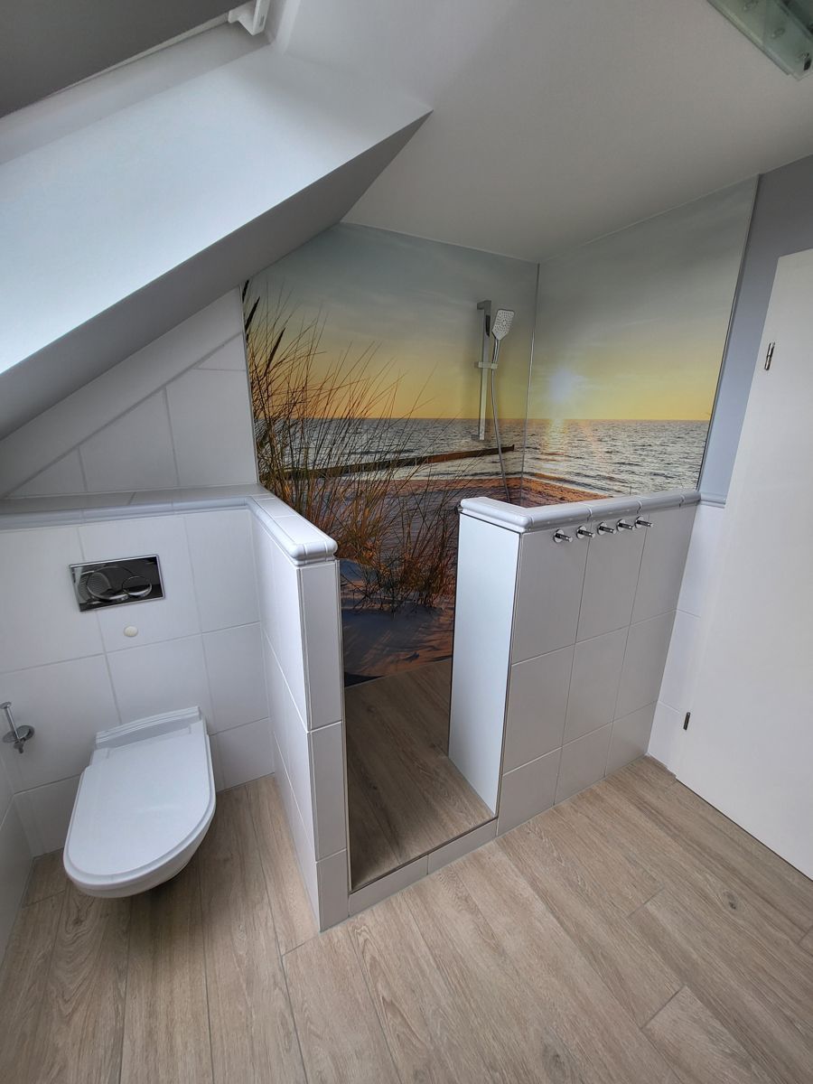 Badezimmer mit Toilette und Dusche, Holzboden, schräger Decke und Wandgemälde mit Meeresmotiv.