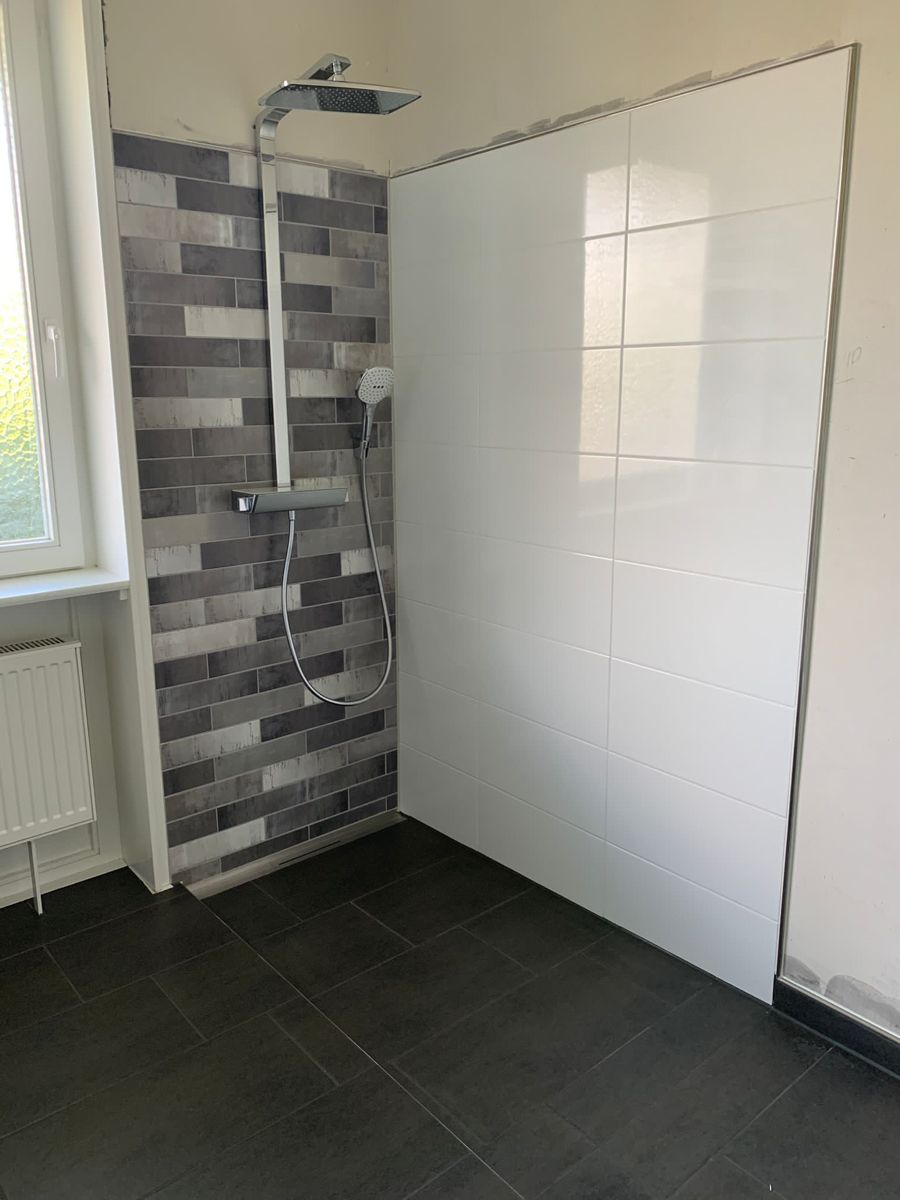 Badezimmer mit dunklem Boden, weiß und grau gefliesten Wänden, Duschkopf und Fenster.