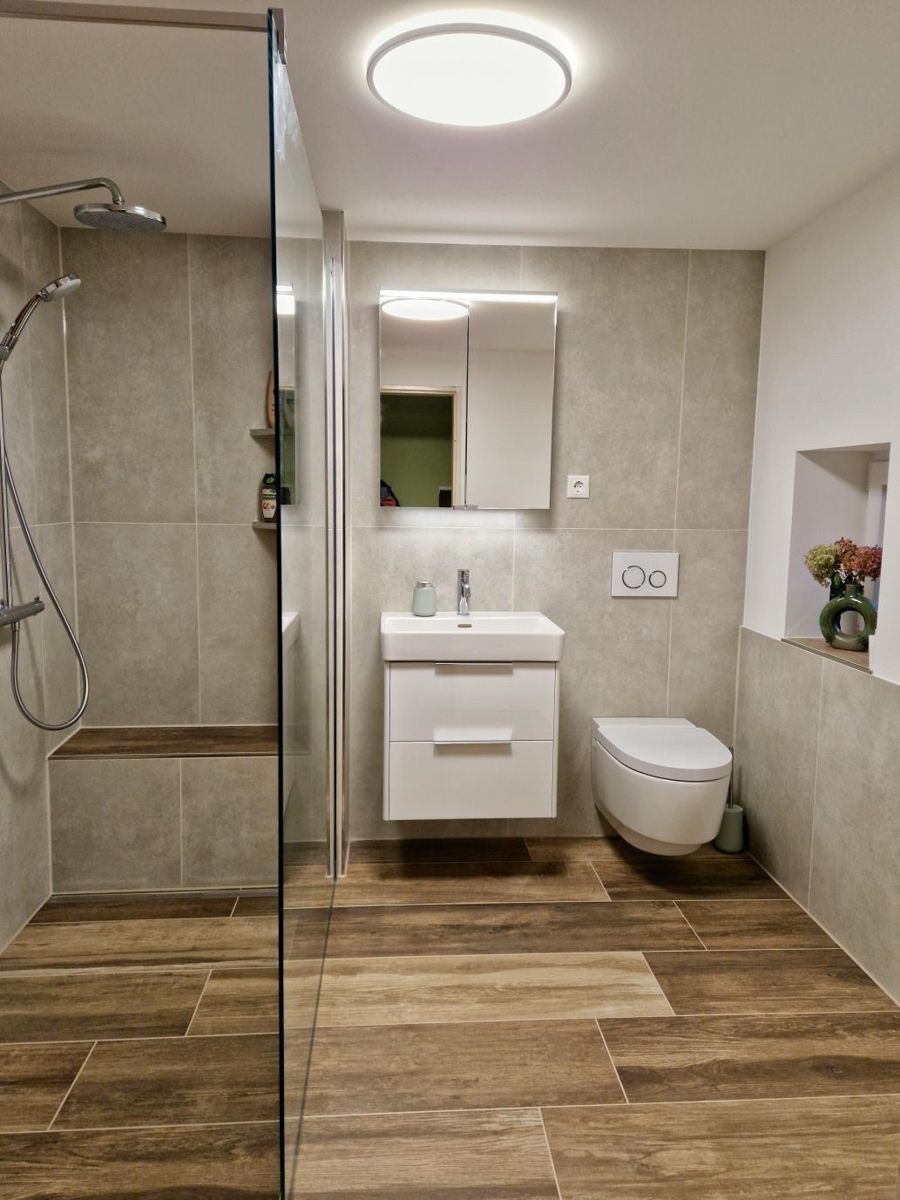Modernes Badezimmer mit Fliesenboden in Holzoptik, grau gefliesten Wänden.