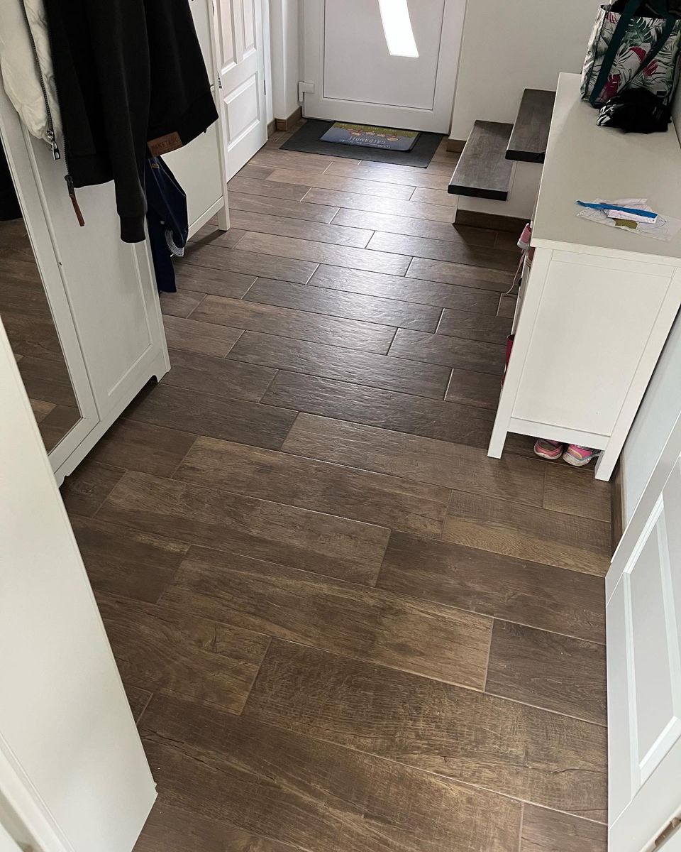 Brauner Holzboden in einem Flur mit weißen Schränken, einer Bank und einer Tür im Hintergrund.