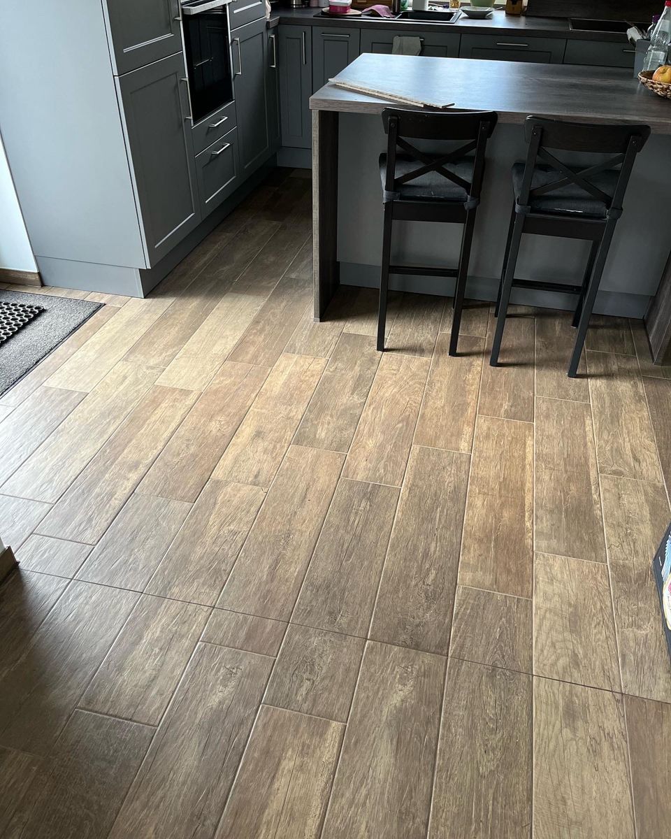 Holzoptik-Bodenbelag in einer Küche mit grauer Kochinsel und zwei Barhockern.