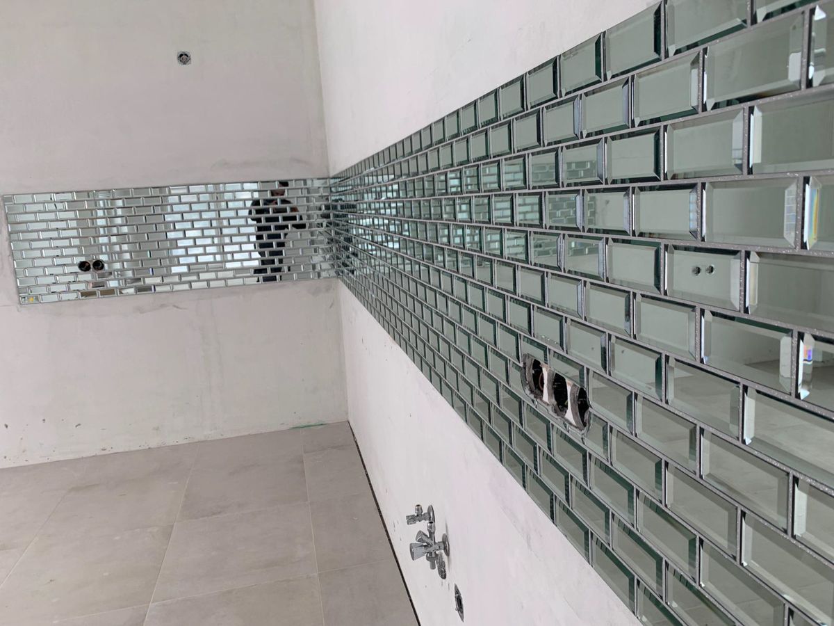 An einer weißen Wand in einer Ecke wird eine Küchenrückwand aus verspiegelten Metrofliesen angebracht.