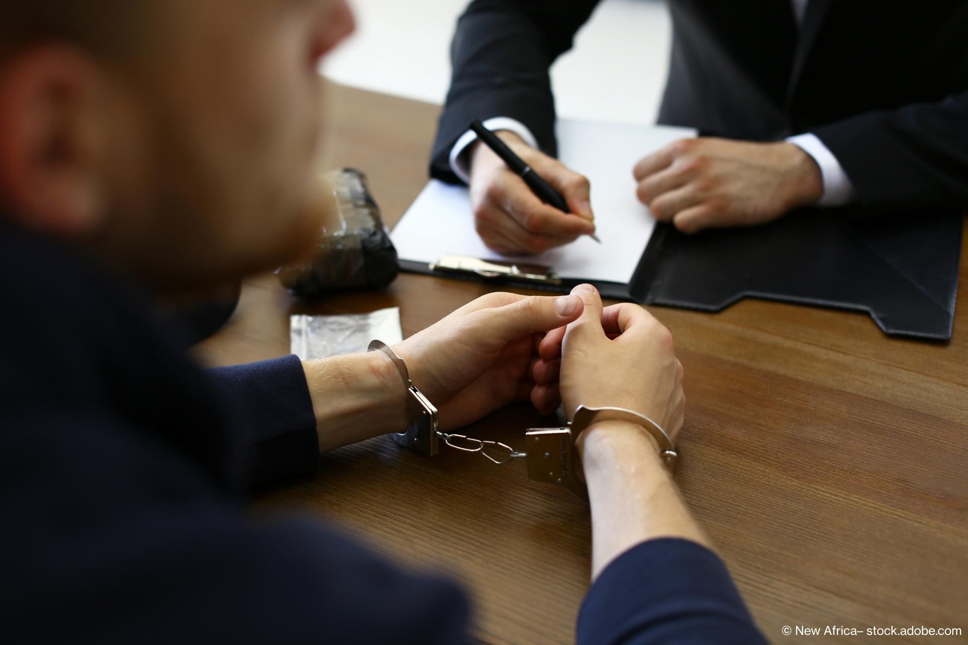 Person mit Handschellen an einem Tisch mit seinem Rechtsanwalt