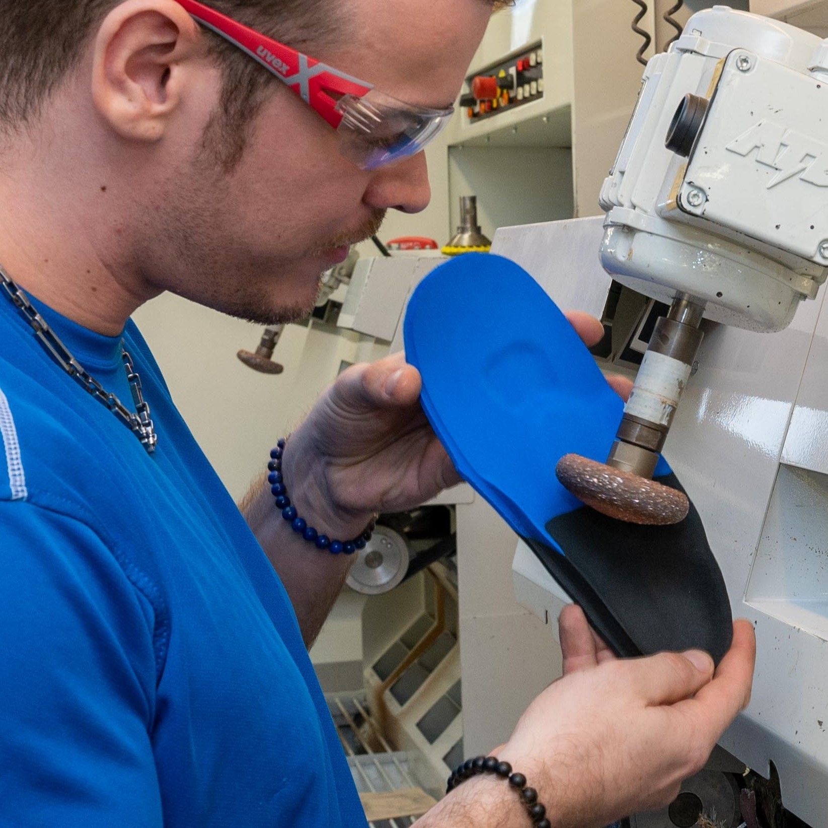 Ein Mann mit Brille und blauem Hemd arbeitet an einem Schuh
