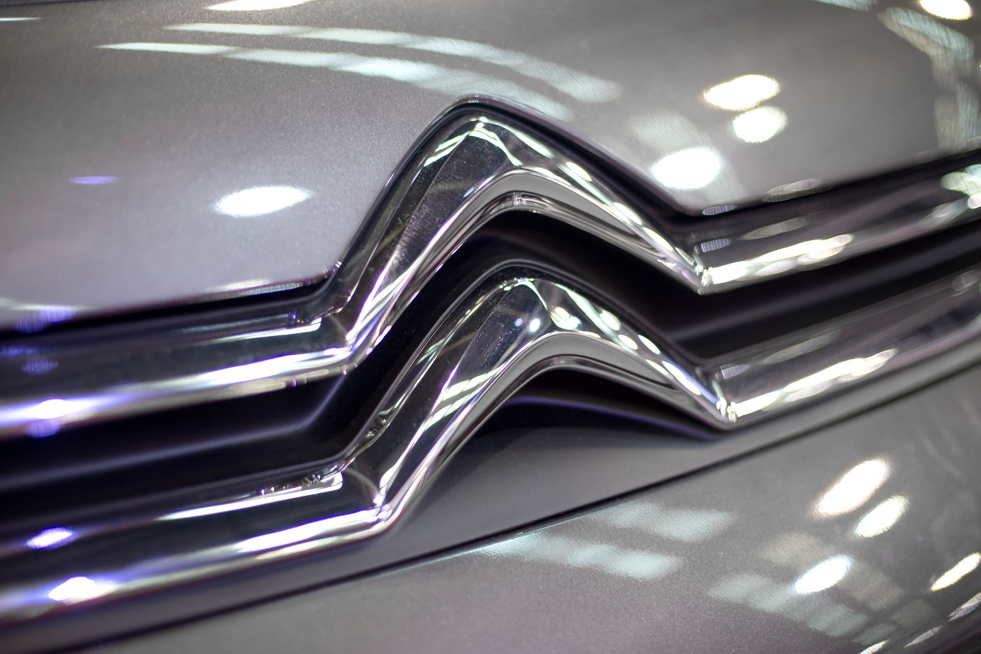 Gros plan sur le logo argenté de Citroën, un emblème chromé en forme de chevron, sur la carrosserie grise d'une voiture.